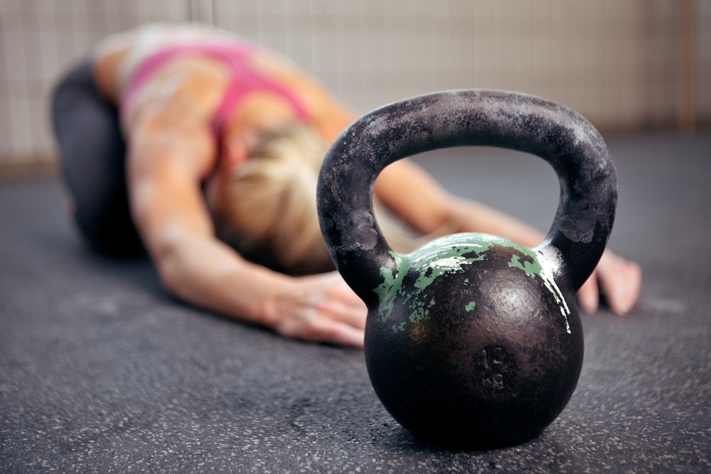 Young woman stretching her back after a heavy kettlebell workout in a gym